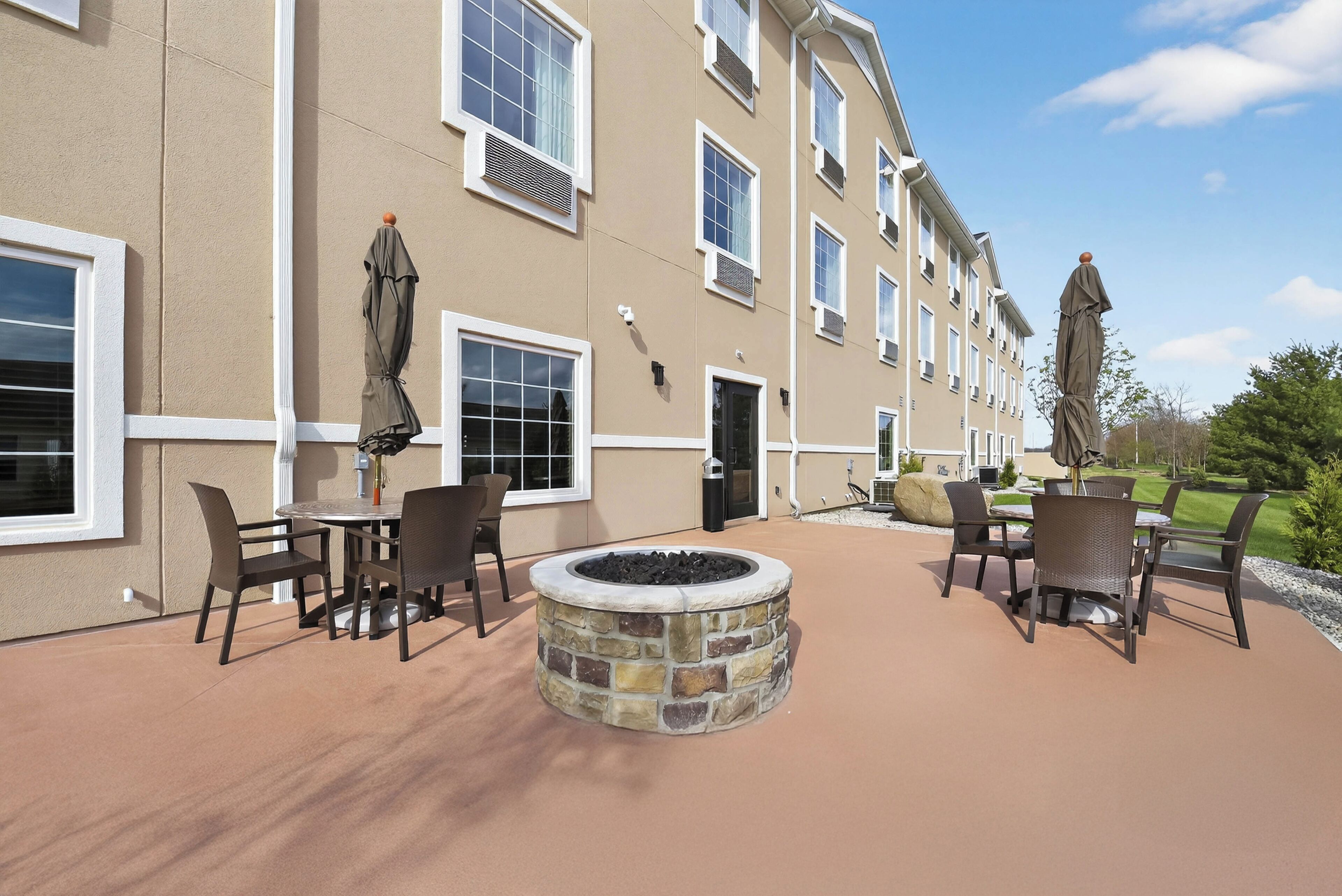 A patio area with outdoor seating, a stone fire pit, and a building with multiple windows and a door.