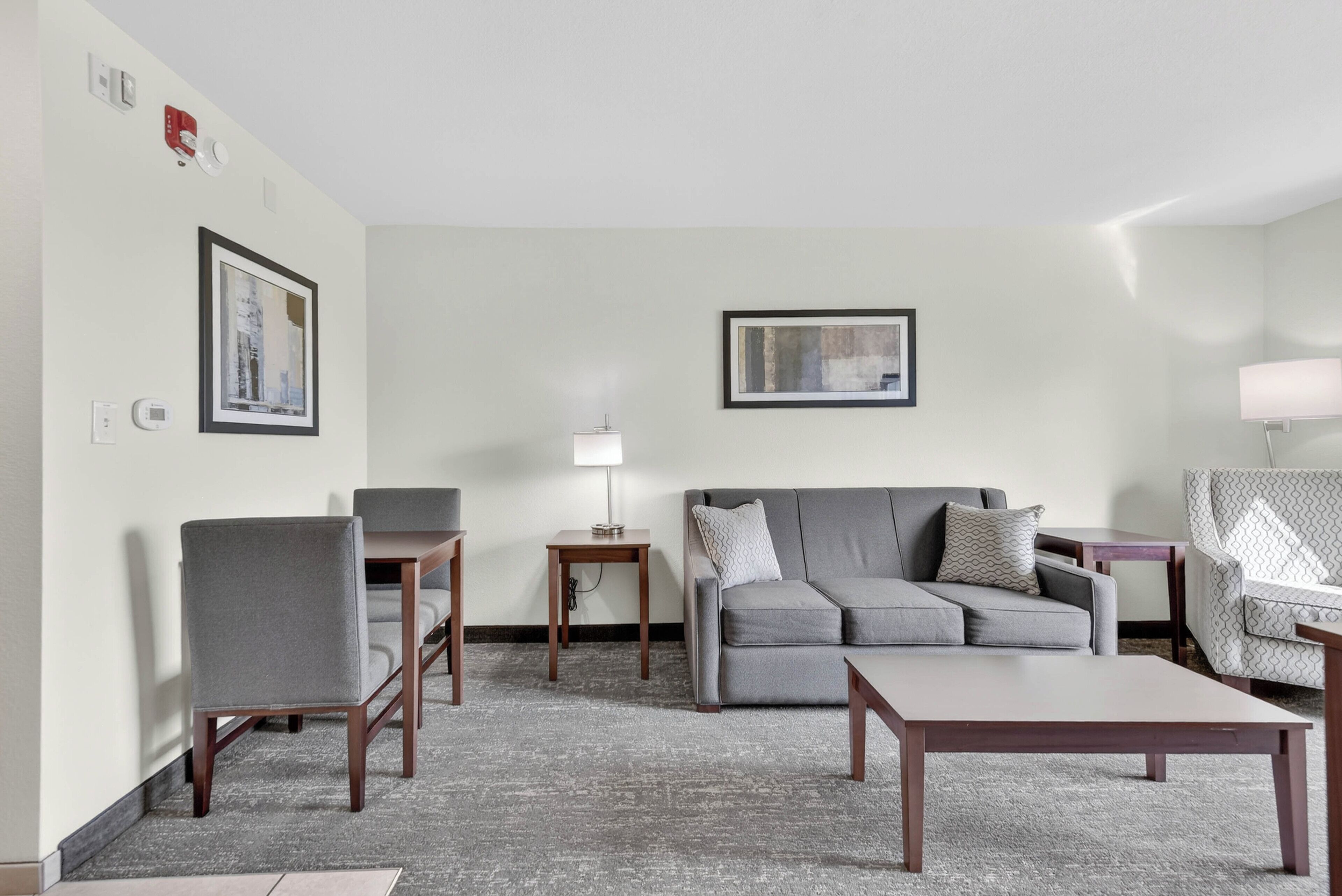 A modern living room with a grey sofa, two armchairs, a coffee table, a side table with a lamp, and framed artwork on the walls.