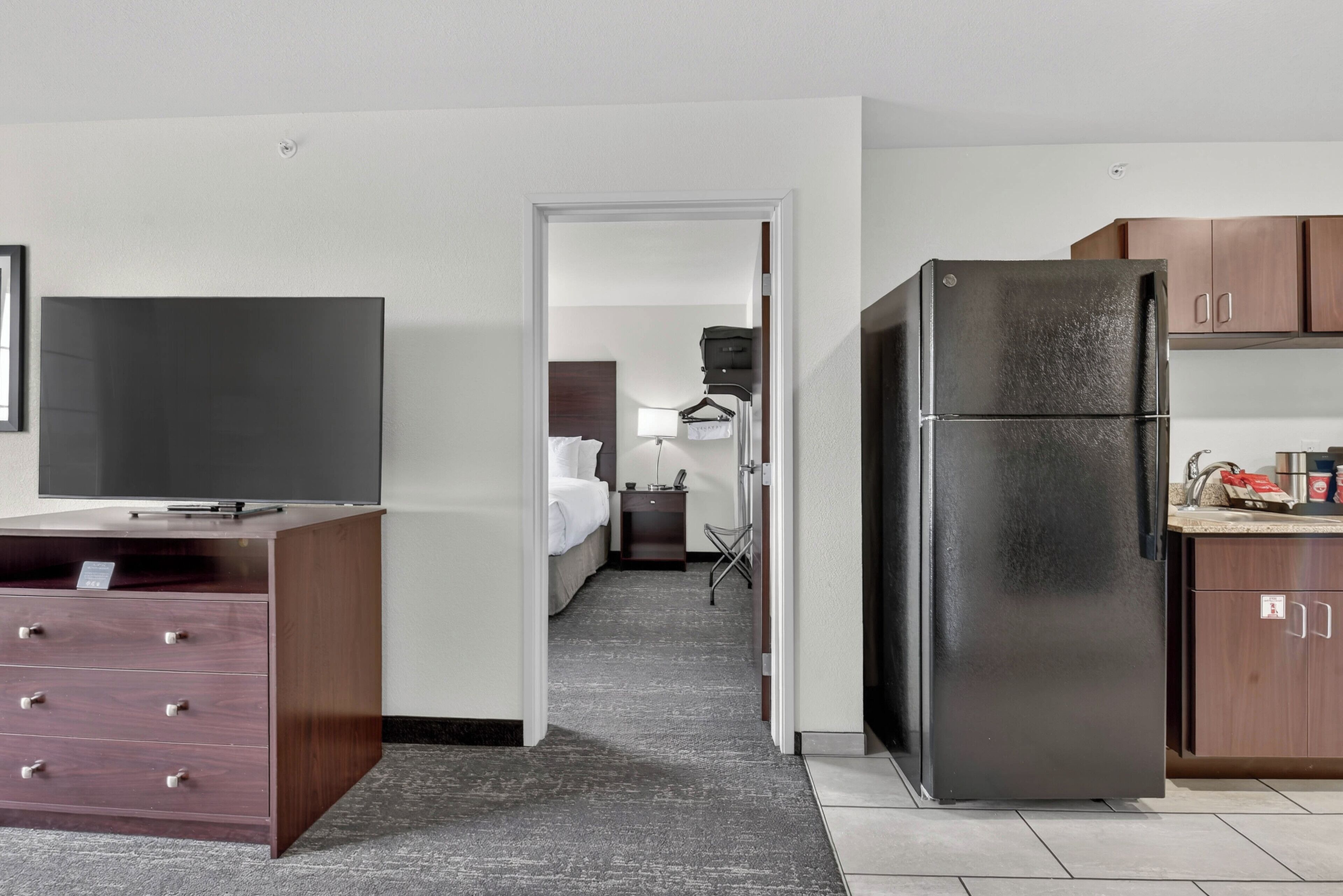 Une chambre d’hôtel équipée d’une kitchenette, d’un téléviseur à écran plat, d’une commode en bois et d’un lit.