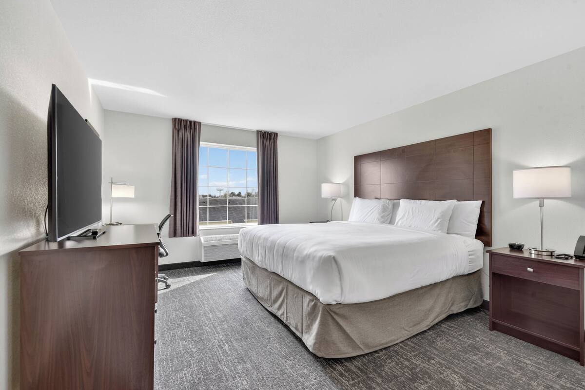 A hotel room with a large bed, a flat-screen TV, a desk, and a window with curtains.