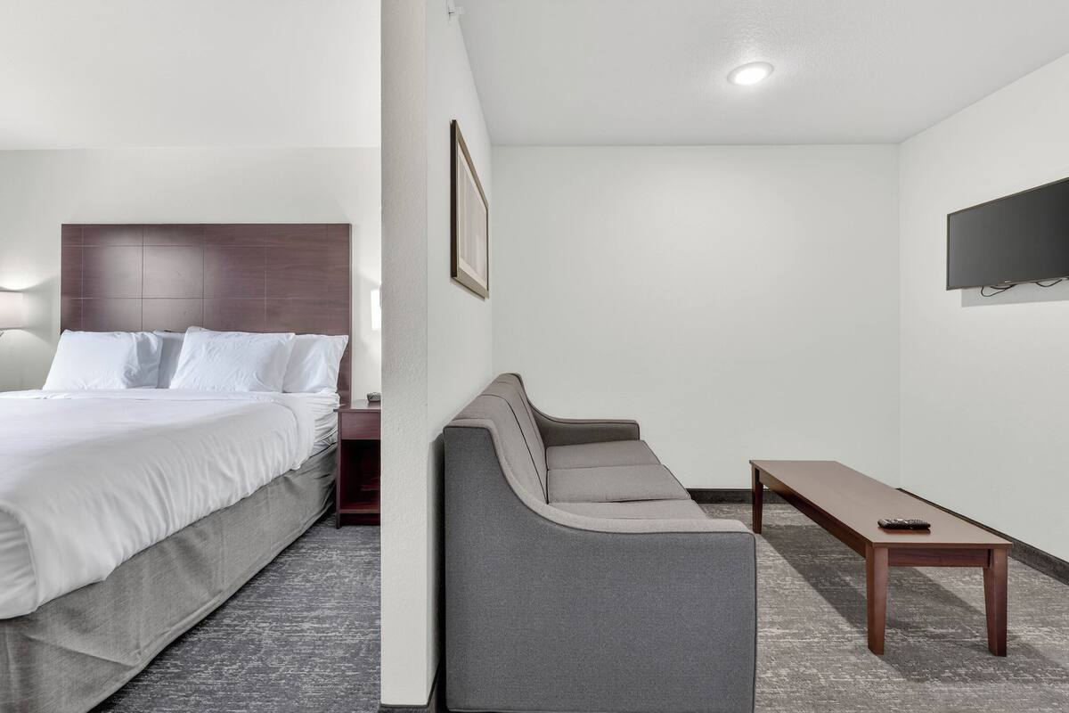 A hotel room with a bed, a sofa, a small table, and a TV mounted on the wall.