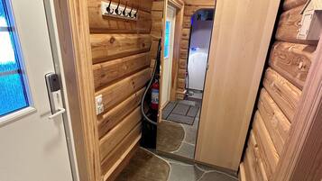 A wooden cabin interior with a door, a window, a fire extinguisher, and a small shelf.