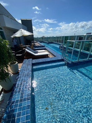 A rooftop infinity pool with clear blue water, lounge chairs, and potted plants. - Edificio Promenade II Apt 1102-Mandi (Maceio)