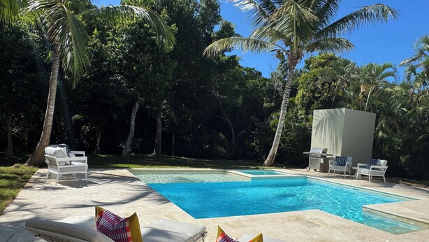 Une piscine dotée de chaises longues et d’un espace barbecue, le tout entouré de palmiers et de verdure.