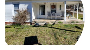 A white single-story house with a front porch, two chairs, and a small garden area. - Entire House Quite Neighborhood (Kannapolis)