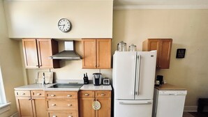 Eine Küche mit Holzausstattung, einer Edelstahl-Dunstabzugshaube, einem Kühlschrank, einem Geschirrspüler, einer Kaffeemaschine und einer Wanduhr.