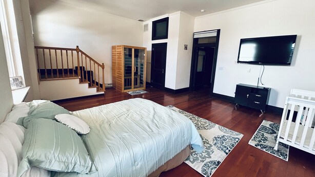 Ein geräumiges Schlafzimmer mit einem großen Bett, einem an der Wand montierten Fernseher, einem Kleiderschrank und einer Treppe, die in einen weiteren Raum führt.