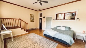 Ein Schlafzimmer mit einem Bett, einem Schreibtisch mit Computer, einer Treppe und einem Deckenventilator.