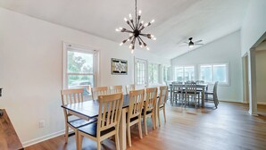 Un vaste espace dédié à la salle à manger, avec des tables et des chaises en bois, de grandes fenêtres et un ventilateur de plafond.