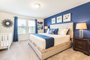 A bedroom with a bed, a nightstand, a crib, and a window with curtains.