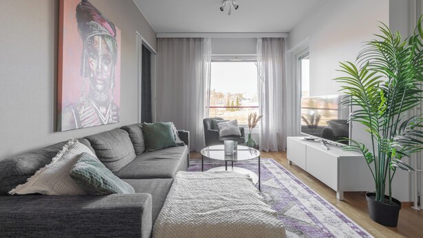 A modern living room with a grey sofa, a coffee table, and a large window with curtains. - Homelike 1BR Apt. with Sauna & Parking (Kuopio)