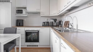 A modern kitchen with white cabinets, a built-in oven, a microwave, a coffee maker, and a sink. - Homelike 1BR Apt. with Sauna & Parking (Kuopio)