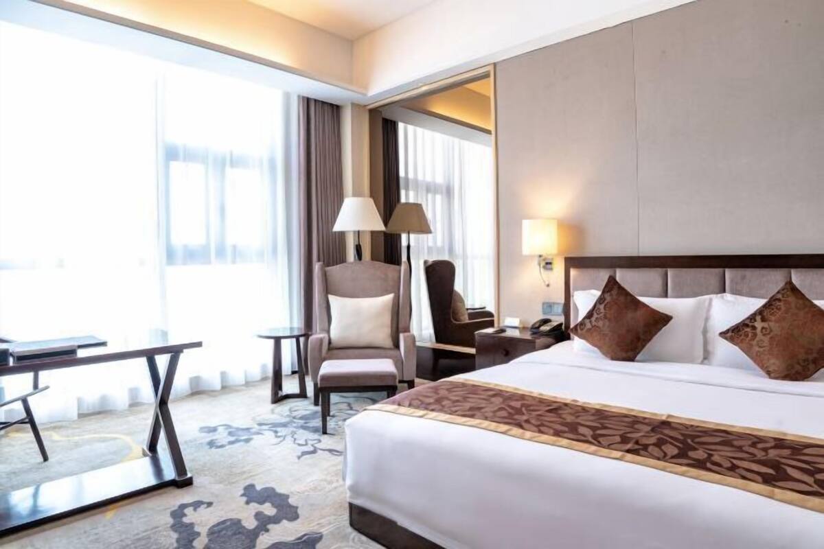 A hotel room with a large bed, two armchairs, a desk, and a lamp.