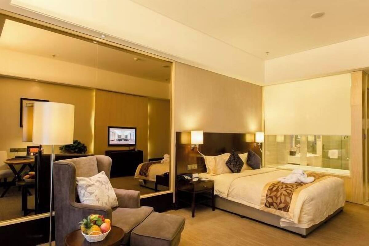 A hotel room with a bed, a desk, a chair, a TV, and a mirror.
