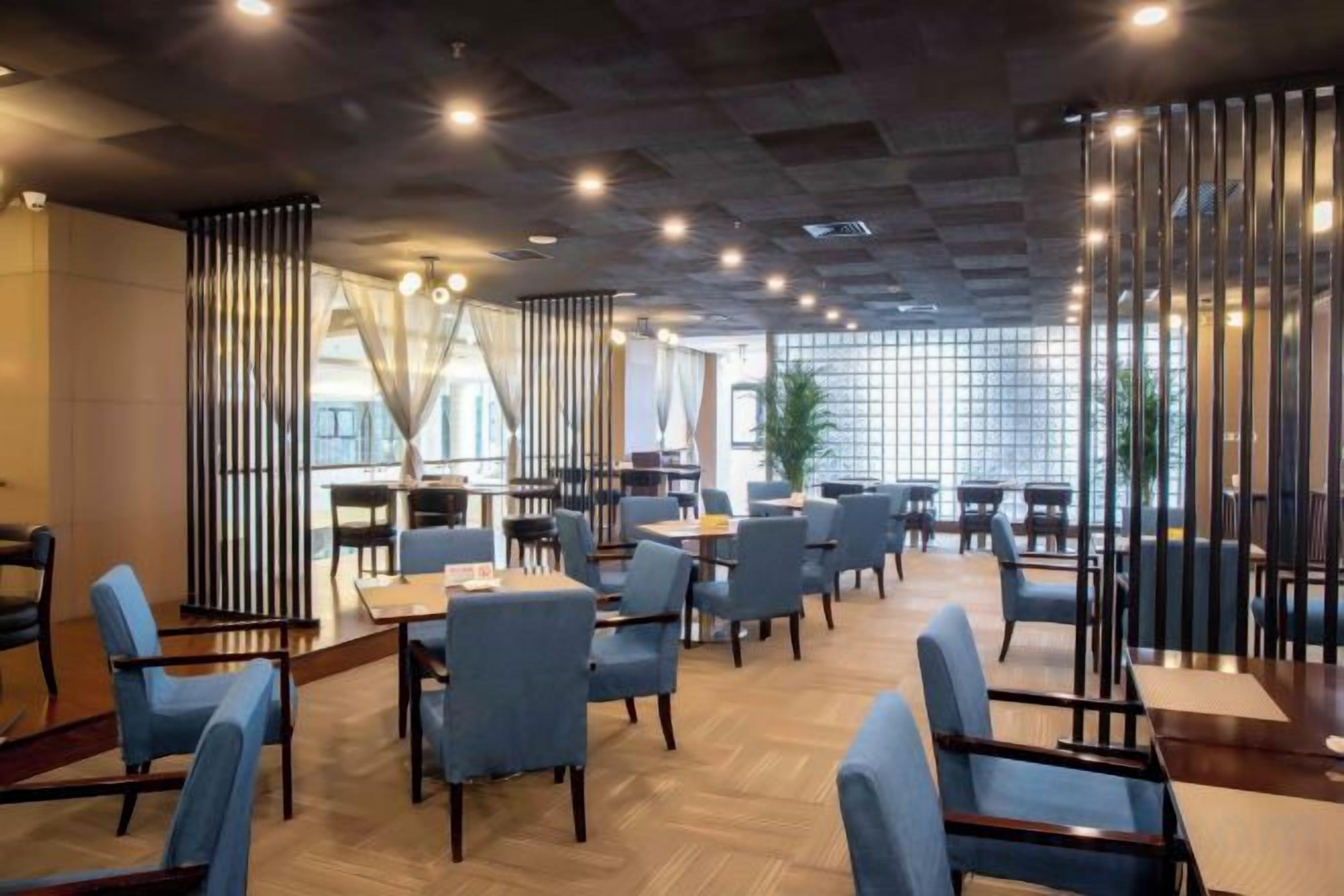 A modern restaurant interior with high tables and chairs, a wooden floor, and a view through large windows.