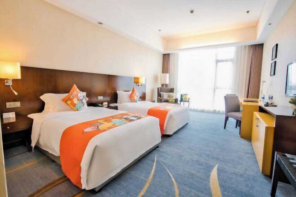 A hotel room with two beds, a desk, a chair, and a TV.