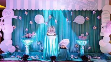 A stage with a teal curtain backdrop, a central floral arrangement, and decorative elements like balloons and a sign.