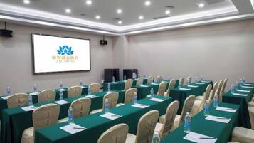 A conference room with rows of tables, chairs, and a projection screen displaying a logo.