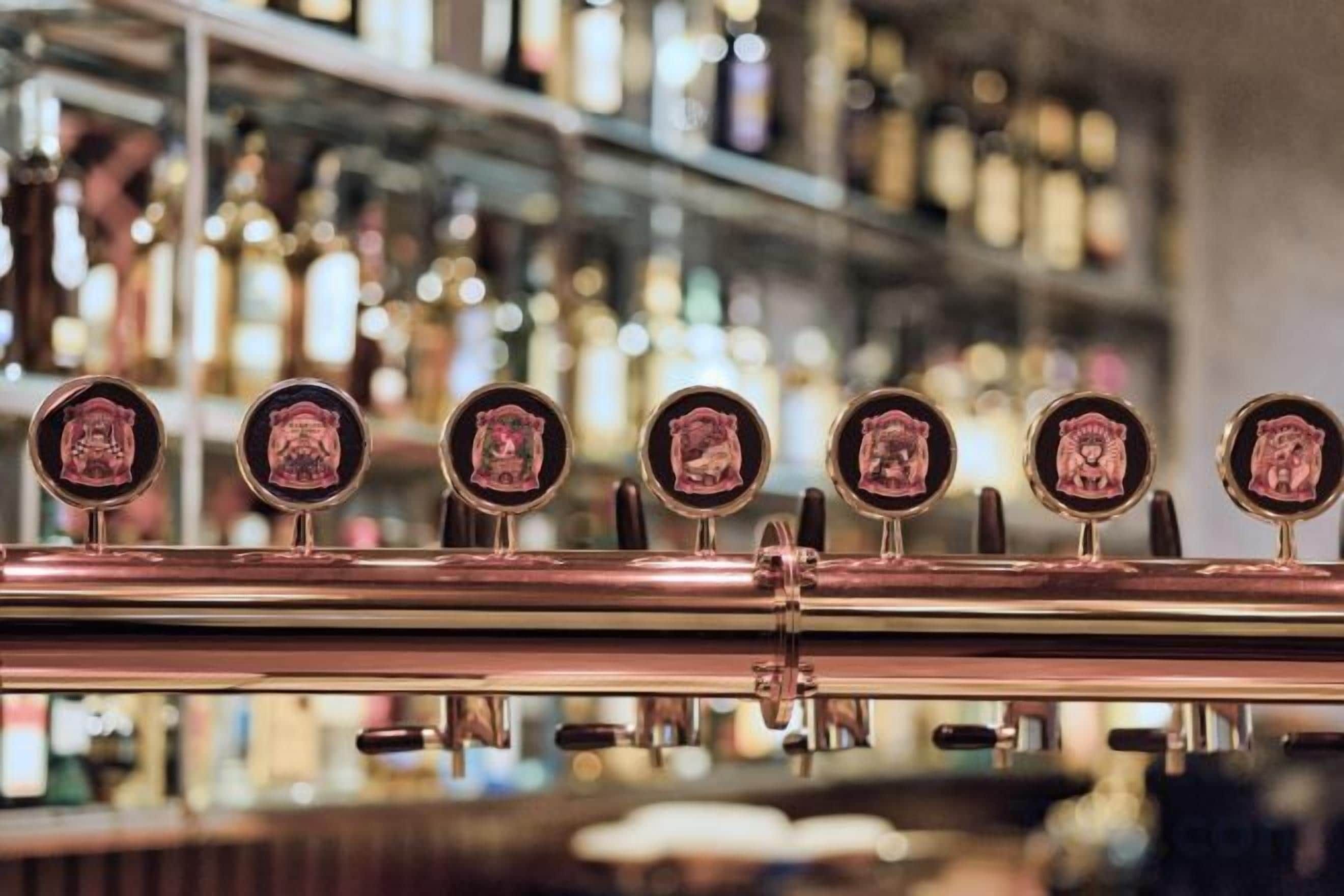 Un bar con una fila de grifos y un fondo borroso de estanterías llenas de botellas.