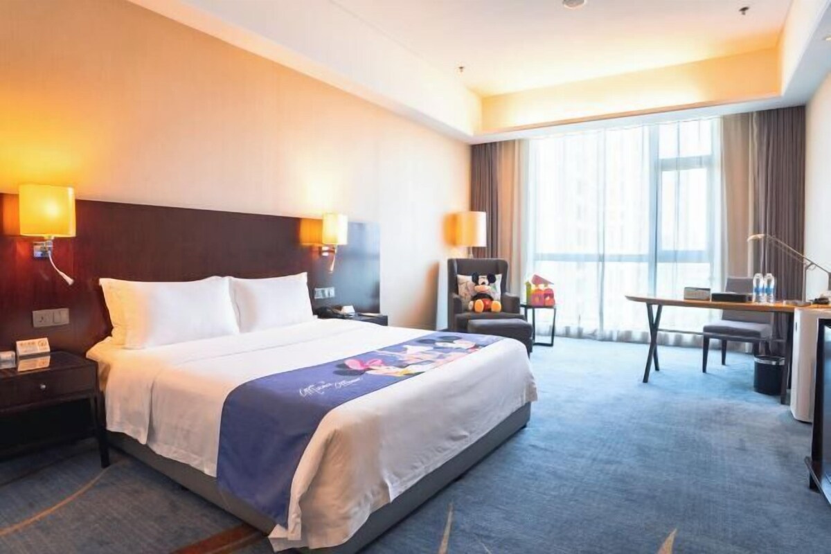 A hotel room with a large bed, bedside lamps, a desk, and a chair.