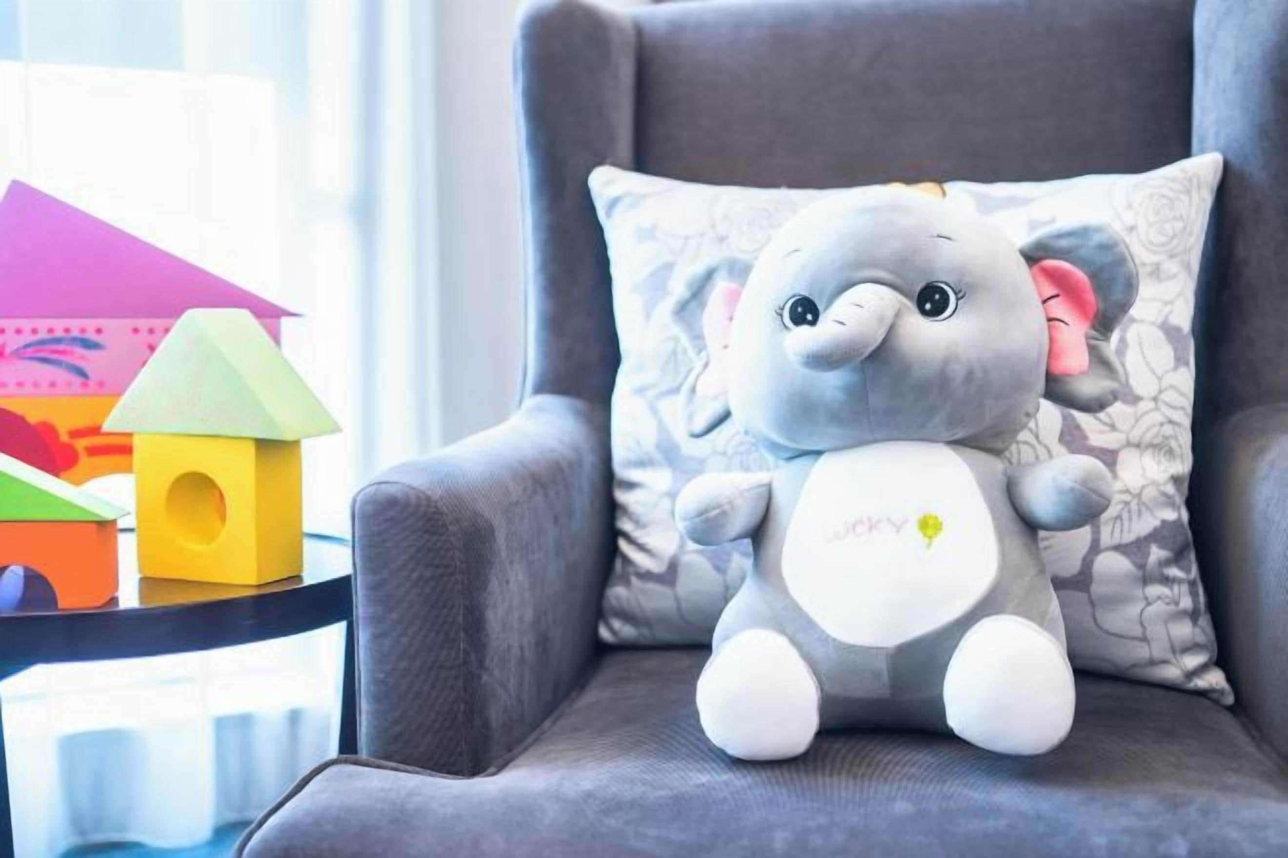 Un peluche de elefante sobre un sillón gris con un cojín estampado de flores.