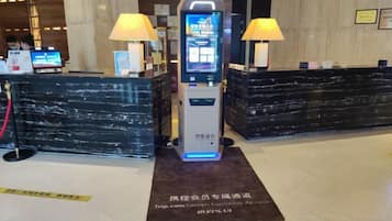 A reception area with a digital check-in kiosk, two lamps, and a marble reception desk.