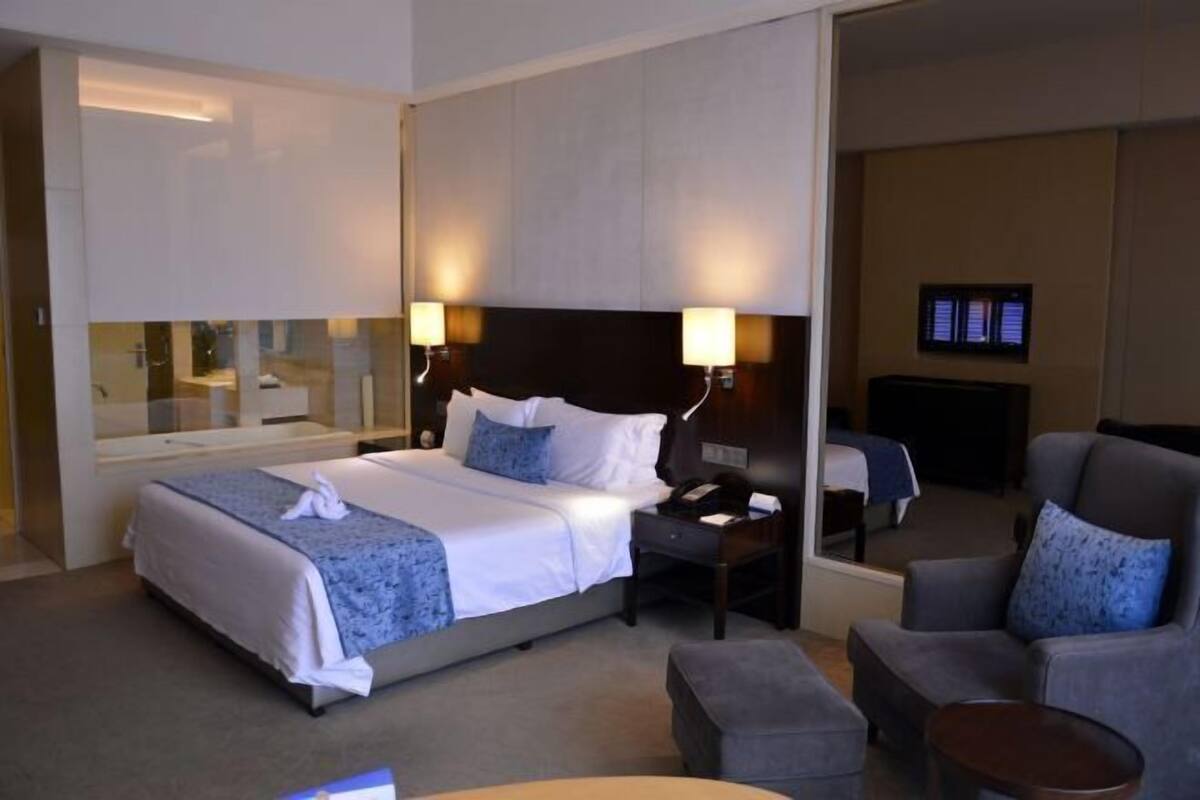 A hotel room with a bed, bedside tables, a chair, a small table, and a TV.
