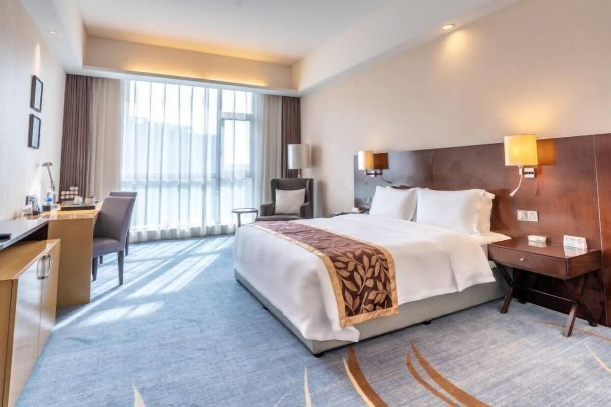 A hotel room with a bed, desk, chair, and large windows.