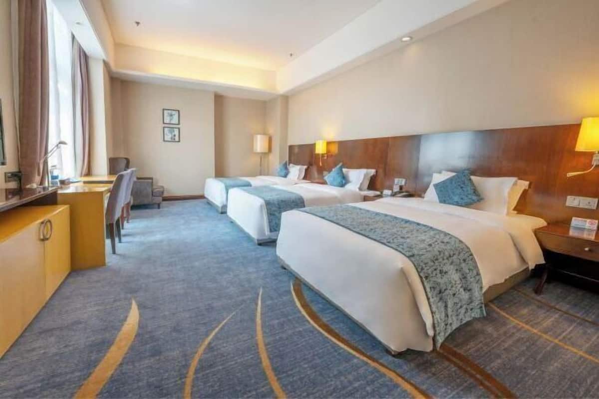 A hotel room with two beds, a desk, a chair, and a TV.