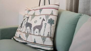 Una habitación con un sofá verde, un cojín estampado y una lámpara de pie.