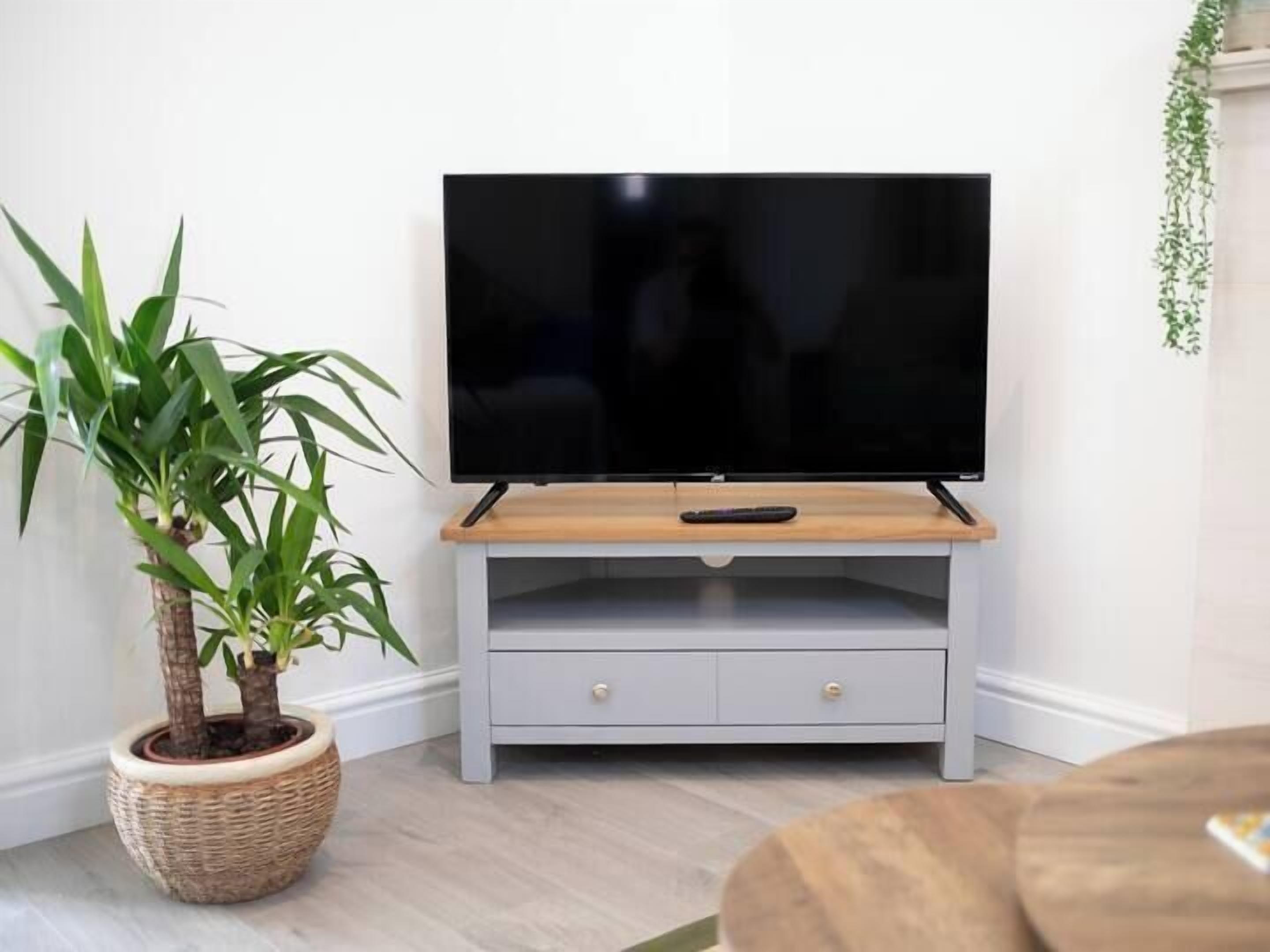 A flat-screen TV on a light grey wooden stand with a remote control on it.