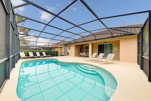 A swimming pool with a glass enclosure, lounge chairs, and a building with a tiled roof.