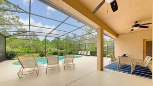 A covered outdoor area with a pool, lounge chairs, and a table.
