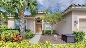 A two-story house with a front porch, a palm tree, and a small garden.