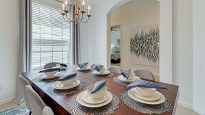 A dining room with a wooden table set for six, a chandelier, and a view into another room.