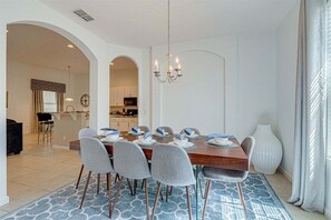 A dining area with a wooden table, grey chairs, a chandelier, and a patterned rug.