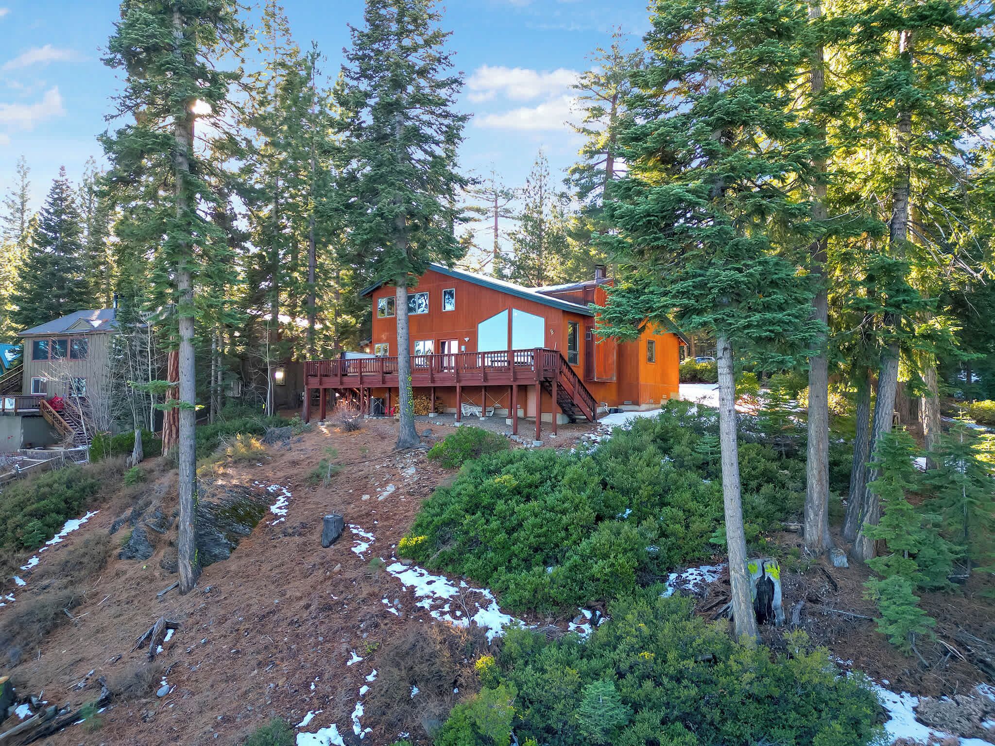 Une cabane dotée d’une terrasse, entourée d’une forêt dense et de quelques zones enneigées.