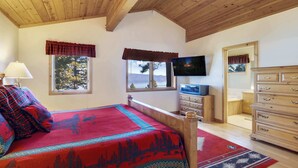 Une chambre à coucher comprenant un lit, une commode, un téléviseur et une fenêtre donnant sur des arbres.