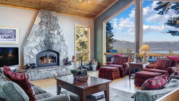 Un salon chaleureux avec une cheminée en pierre, des meubles à motifs écossais et une grande fenêtre donnant sur les montagnes.