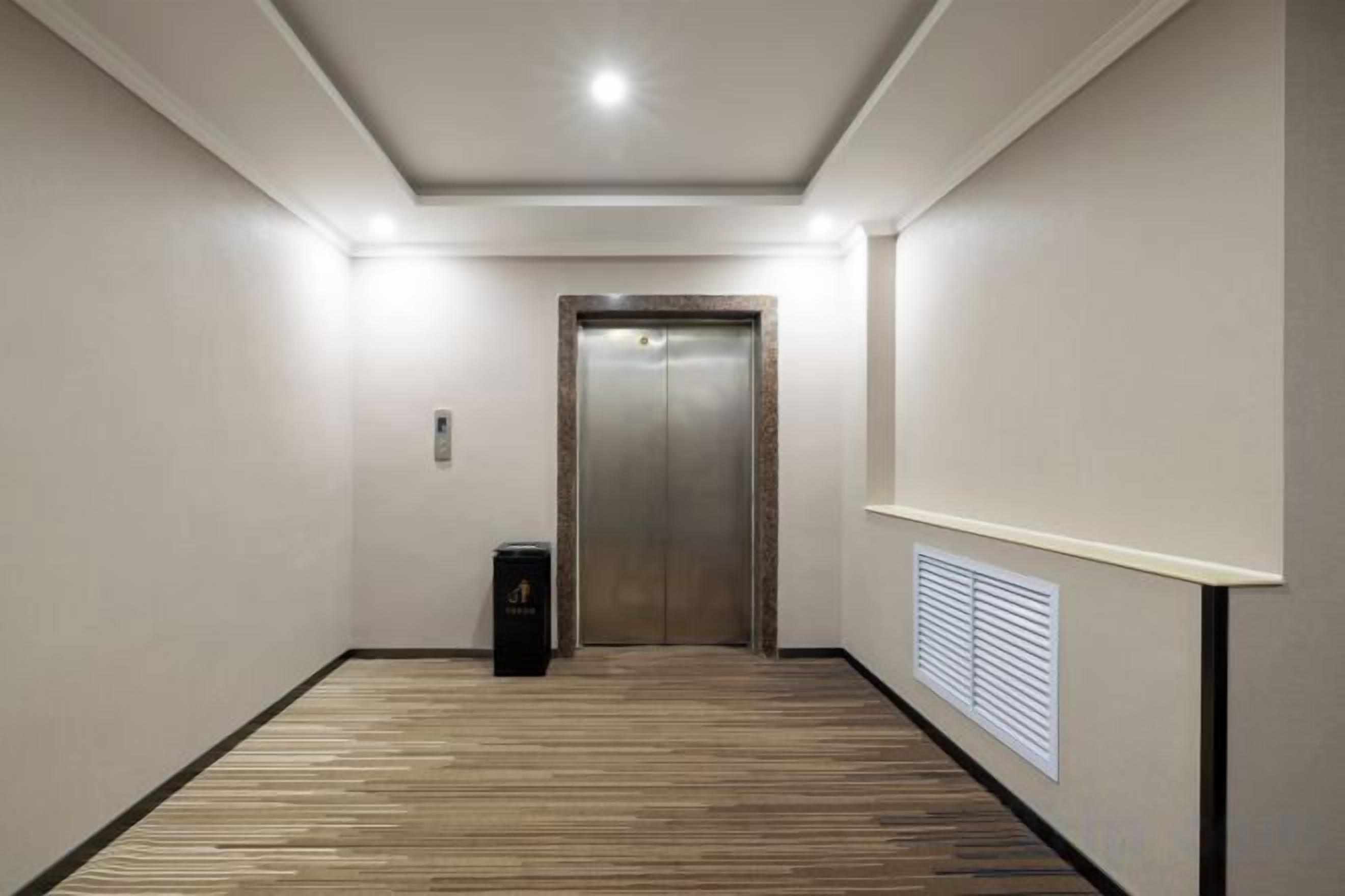 Un couloir avec un plancher en bois, une porte au fond et une poubelle sur la gauche.