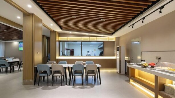 A modern dining area with a long table and chairs, a wooden ceiling, and a kitchen area visible through a glass partition. - GreenTree Inn (Affiliated Hospital of University of Traditional Chinese Medicine) (Taiyuan)