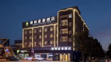 A multi-story hotel with illuminated signage, a ground-level restaurant, and a parking area.