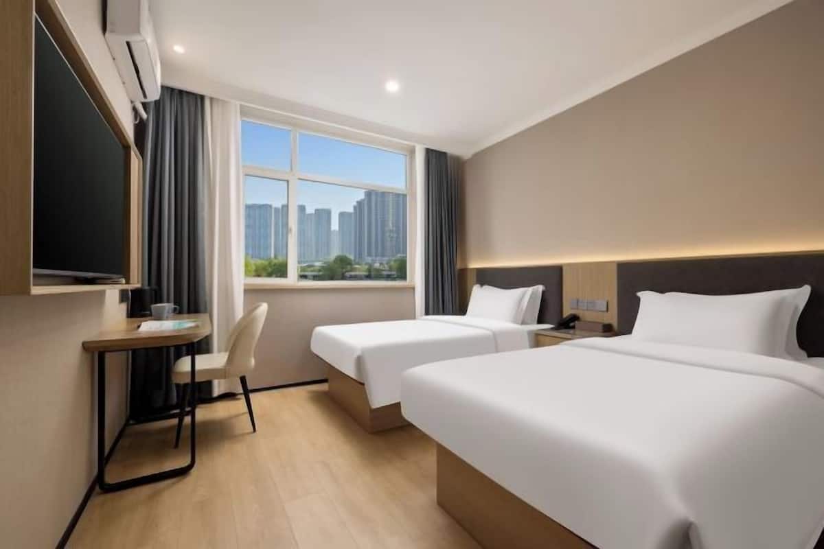 A hotel room with two beds, a desk, a chair, a TV, and a window with a city view.