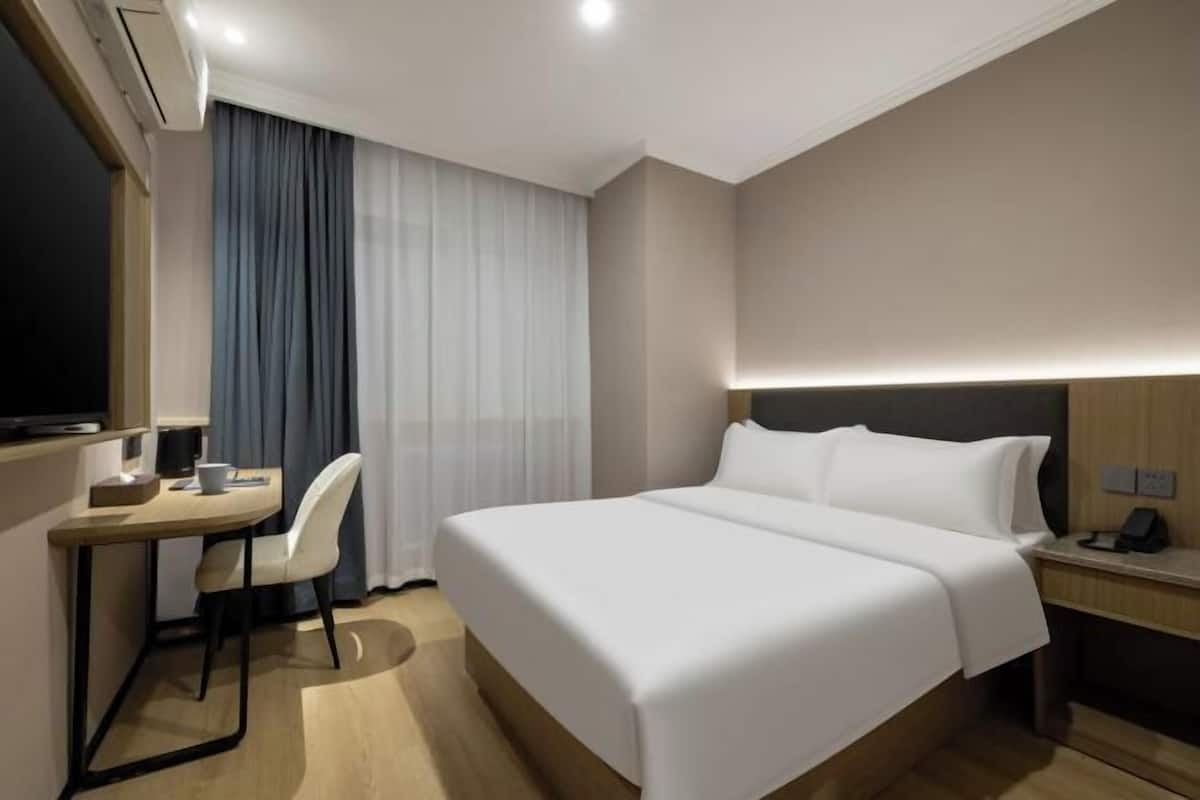 A hotel room with a bed, a desk, a chair, a TV, and a bedside table.