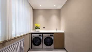 A laundry room with two washing machines, a sink, and a window with curtains.