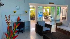 A reception area with a desk, office chair, and wicker furniture. There is a clock on the wall and a view of an outdoor patio with a pool and chairs. - Whole house: villa in Llano Del Pozo, Colombia (Llano Del Pozo)