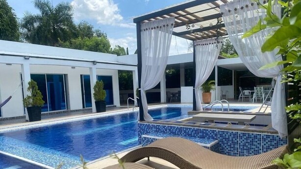 A swimming pool with a separate hot tub area, surrounded by a covered seating area with white curtains. - Whole house: villa in Llano Del Pozo, Colombia (Llano Del Pozo)