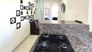 A modern kitchen with a granite countertop, a gas stove, and a flat-screen TV mounted on the wall.