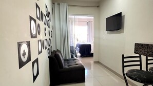 A living room with a sofa, a TV mounted on the wall, and a dining area with a table and chairs.