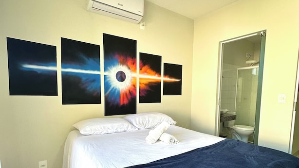 A hotel room with a bed, a shower, and four wall-mounted paintings.